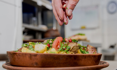 Chef cooks fried potatoes with pieces of meat in a restaurant kitchen