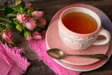 Fototapeta na wymiar pink knitted cup of tea with heart on dark background decorated with pink roses