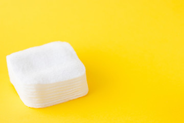 Cotton white square napkins for woman hygiene on a yellow background. Beauty and body and face care. Flat lay style. Copyspace for text.