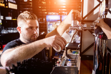 Bartender pouring draft beer at glasses in the bar. Restaurant.