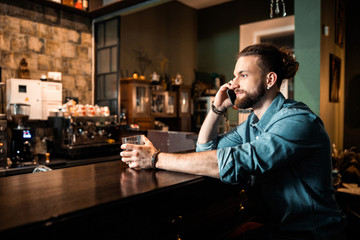 Smiling young guy talking on mobile phone at bar