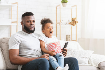 Emotional black father and daughter watching movies together