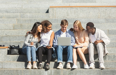 Fototapeta premium Students doing homework on laptop, sitting on stairs in city