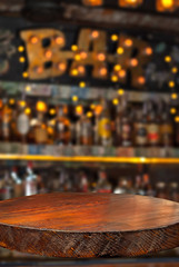 Wooden board on a background of bottles with alcohol. Old bar counter as layout for design. Workpiece for design. Empty place to advertise products. Blurred interior of the bar in the background.