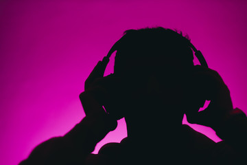 silhouette of a man in headphones isolated on a pink background. Music concept 