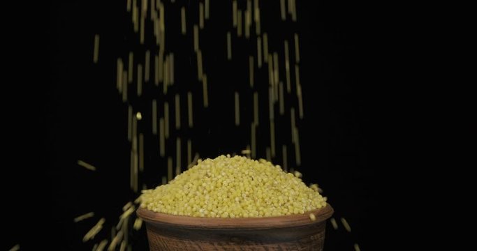 Whole grains of millet fall on a bunch of grains lying in a clay pot and fall out of the pot. Close-up.