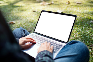 Mockup image of a woman using and typing on laptop with blank white screen , sitting in the outdoors with nature background