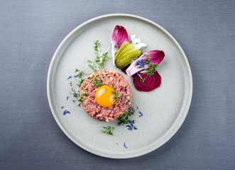 Gourmet tartar raw from beef fillet with yellow of the egg und vegetable as top view on modern design dish - obrazy, fototapety, plakaty