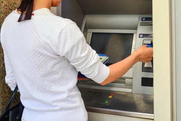 A woman withdraws cash through an ATM using a plastic card.