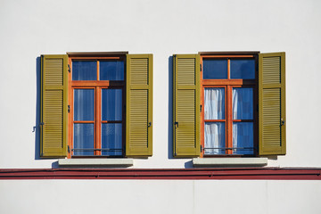 Two italian windows on the bright wall facade with open wooden green shutters