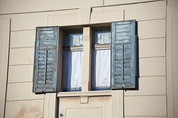 Italian window on the bright beige color wall facade with open wooden shabby paint grey-blue shutters