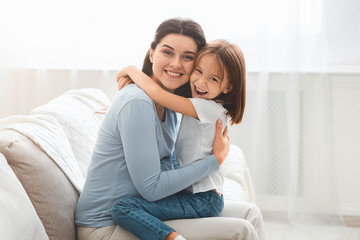 Little daughter and young mother hugging each other at home