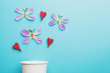 creative spring composition, paper coffee cup, butterflies made of fresh flower petals and red wooden hearts isolated on pastel blue background, copy space