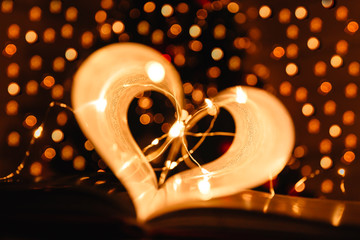 art book novel with sheets in the shape of a heart decorated with bright garland lights background, symbol of love