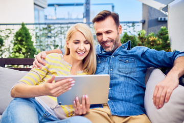 Cheerful couple relaxing together on terrace and using smartphone