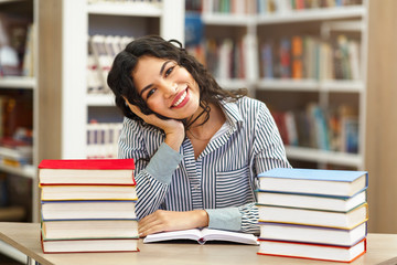 Smiling latina girl sitting at desk in library