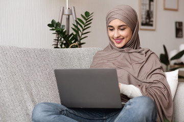 Young muslim woman in hijab working on laptop at home