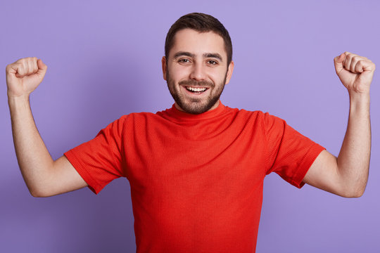 Imag eof excited happy young Caucasian man clenching his fists, celebrating his succses, posing isolated over purple background, looking at camera and screaming happily.People emotions concept.