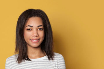 Obraz premium Smiling mixed race young woman in striped shirt on yellow studio background