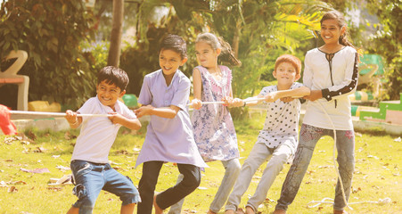 Group of multi racial children playing Tug of war game kindergarten - Multi ethnic kids playing outdoor games againt racism.