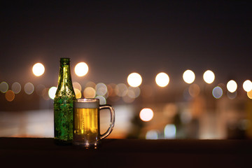 An empty bottle of beer and a glass of beer on a night city lights background