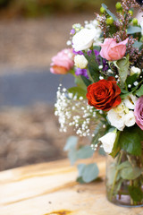A half of colorful bouquet of beautiful bright flowers in a glass bottle standing on the tree trunk in the middle of the forest. Focus on red flower.