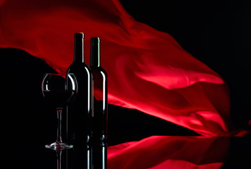 Red wine on a black reflective background. Red satin curtain flutters in the wind.