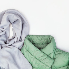 Bright fashion clothes on white background with copy space. Blue wide scarf from fabric and warm down jacket green colored. Flat lay with warm womens clothing. Top view.