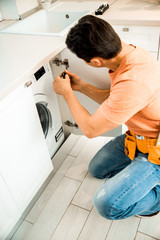 Worker with belt repairing furniture on the kitchen