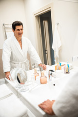 Smiling adult male standing in bathrobe and looking in the mirror