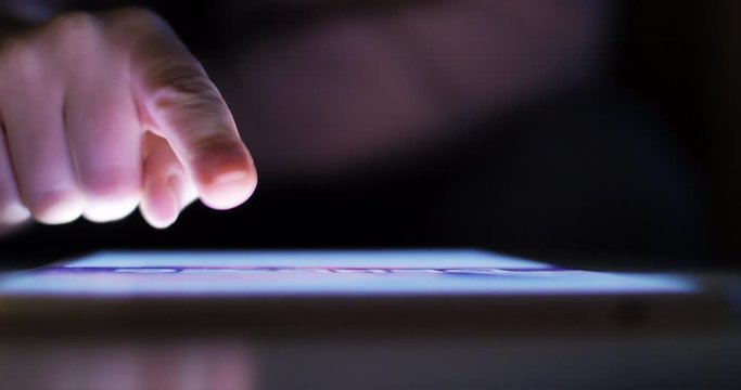 Woman using tablet at night with light from screen. Hand finger swipe and scroll on screen. Woman using tablet for shopping online or social network. Close up 4k footage.