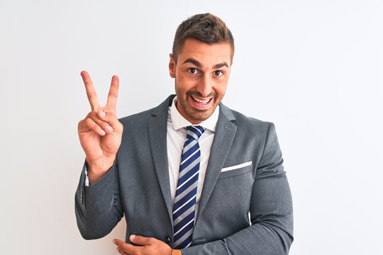 Young handsome business man wearing suit and tie over isolated background smiling with happy face winking at the camera doing victory sign with fingers. Number two.