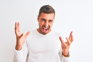 Fototapeta premium Young handsome man wearing white shirt over isolated background crazy and mad shouting and yelling with aggressive expression and arms raised. Frustration concept.