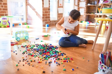 Adorable toddler playing with building blocks toy around lots of toys at kindergarten