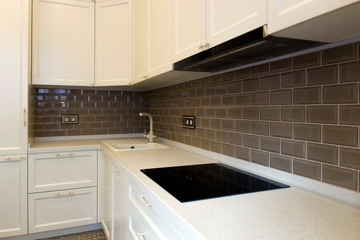Facade of a white, wooden kitchen with a brown apron in brick