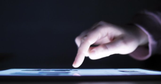 Woman using tablet at night with light from screen. Hand finger swipe and scroll on screen. Woman using tablet for shopping online or social network. Close up 4k footage.
