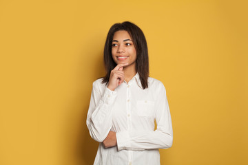 Happy young student woman thinking on yellow background