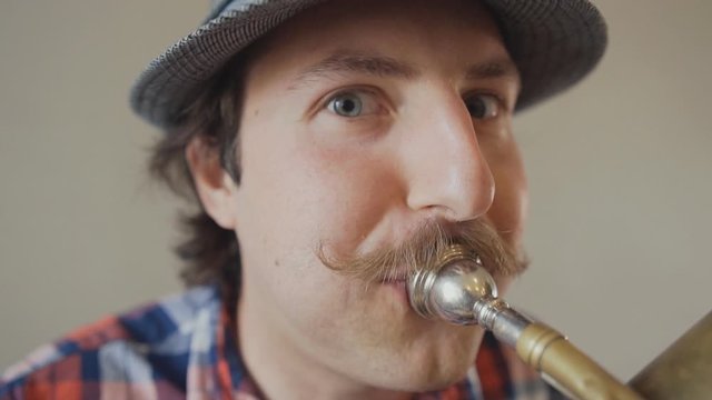 Cheerful young man with a funny mustache and a hat playing on the big tuba. Close up