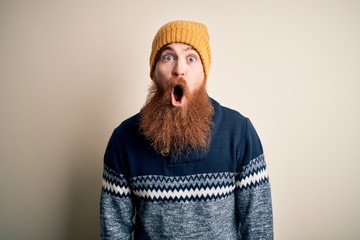 Handsome Irish redhead man with beard wearing winter sweater and wool hat afraid and shocked with...