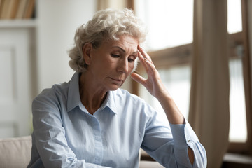Stressed mature elderly grandmother feeling unwell, sitting alone at home.