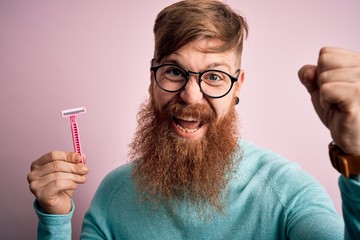 Redhead Irish man with beard holding beauty razor for shaving and skin care over pink background...