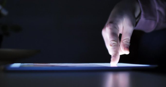 Woman using tablet at night with light from screen. Hand finger swipe and scroll on screen. Woman using tablet for shopping online or social network. Close up 4k footage.