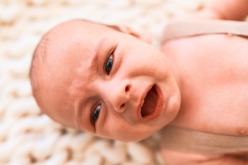 Adorable baby lying down over blanket on the sofa at home. Newborn crying and screaming
