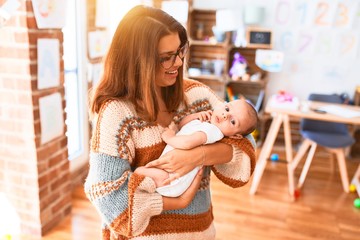 Young beautiful woman and her baby standing at home. Mother holding and hugging newborn