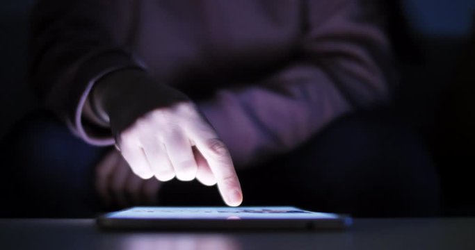 Woman using tablet at night with light from screen. Hand finger swipe and scroll on screen. Woman using tablet for shopping online or social network. Close up 4k footage.