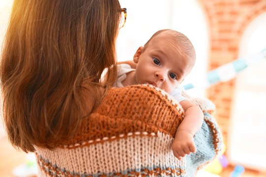 Young beautiful woman and her baby standing at home. Mother holding and hugging newborn