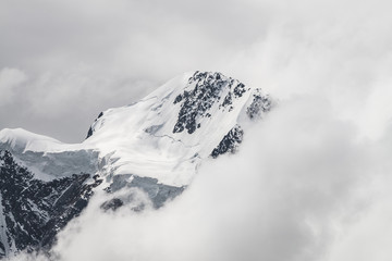 Fototapeta na wymiar Atmospheric minimalist alpine landscape with massive hanging glacier on snowy mountain peak. Big balcony serac on glacial edge. Low clouds among snowbound mountains. Majestic scenery on high altitude.