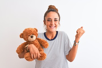 Young beautiful redhead woman holding stuffed teddy bear over isolated background screaming proud...