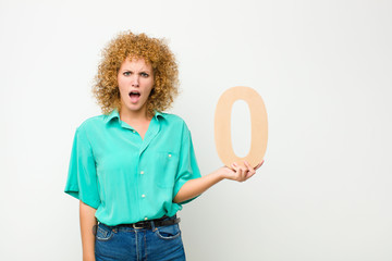 young pretty afro woman confused, doubtful, thinking, holding a number 0.