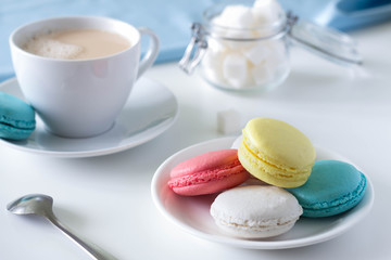 Macarons on a plate and tea with milk on a white table